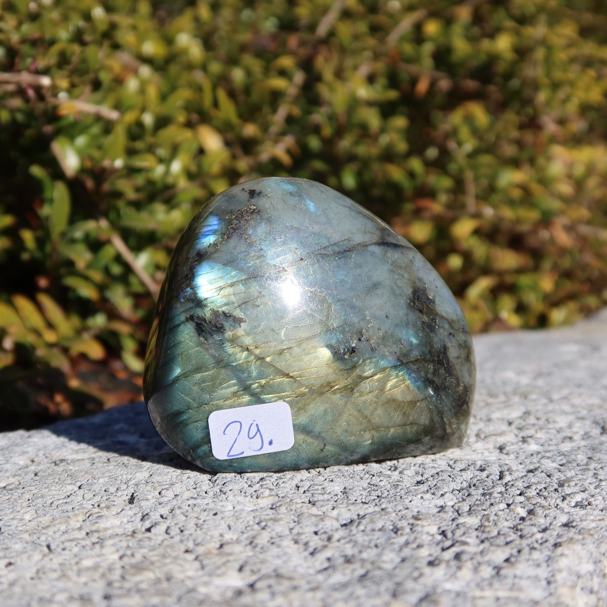 Labradorit Freiform poliert - 5x6cm - Intuition und Kreativität Nr.29 mit schimmernden Farbspielen auf einem Steinuntergrund im Freien.