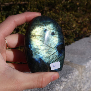 Labradorit Freiform poliert - 7x5cm - Intuition und Kreativität Nr.4 in der Hand vor natürlichem Hintergrund, schimmernde Farben