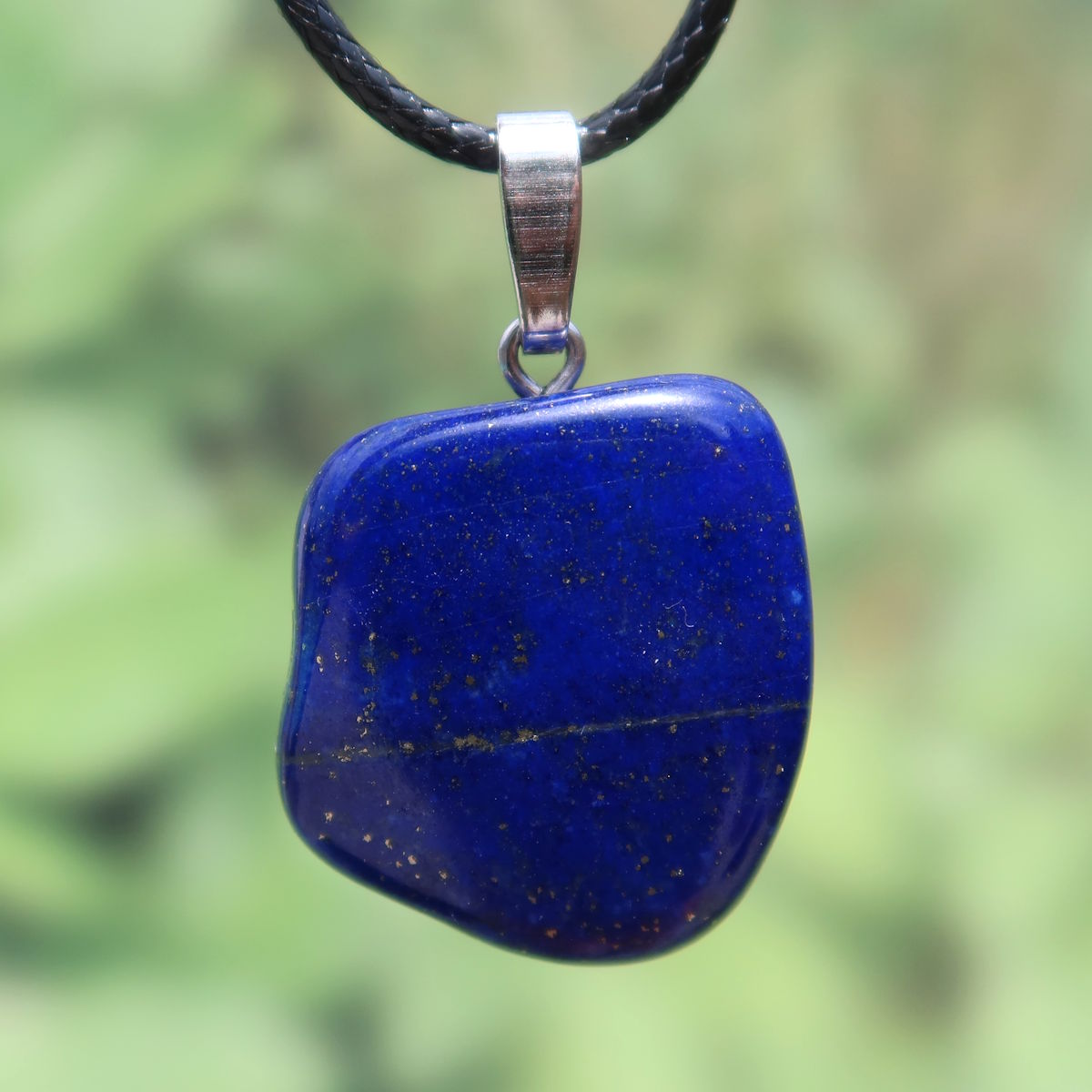 Blauer Lapislazuli Anhänger mit goldenen Sprenkeln und Silberöse, Unikat, steht vor grünem Hintergrund.