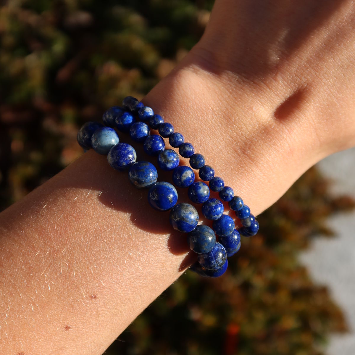 Arm mit Lapislazuli Edelstein Armband - 1 Stück - in Varianten 4-6-8 oder 10mm, zeigt blaue Steine auf Naturhintergrund