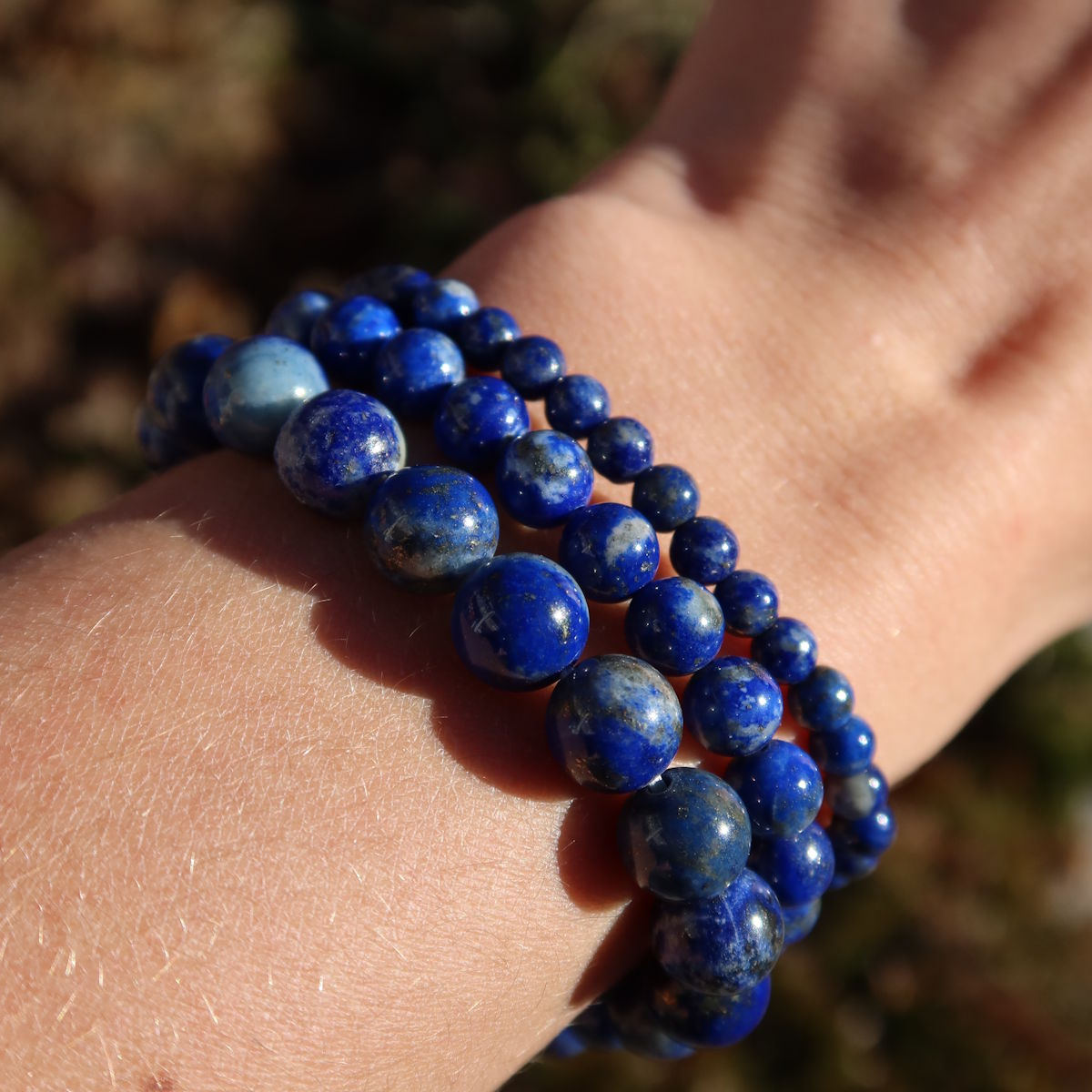 Arm mit Lapislazuli Edelstein Armband - 1 Stück - in Varianten 4-6-8 oder 10mm, zeigt blaue Steine auf Naturhintergrund