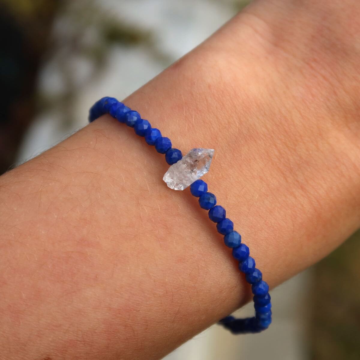 Handmade lapis lazuli and Herkimer diamond bracelet on wrist, featuring deep blue faceted beads and a central Herkimer quartz crystal, 17cm.
