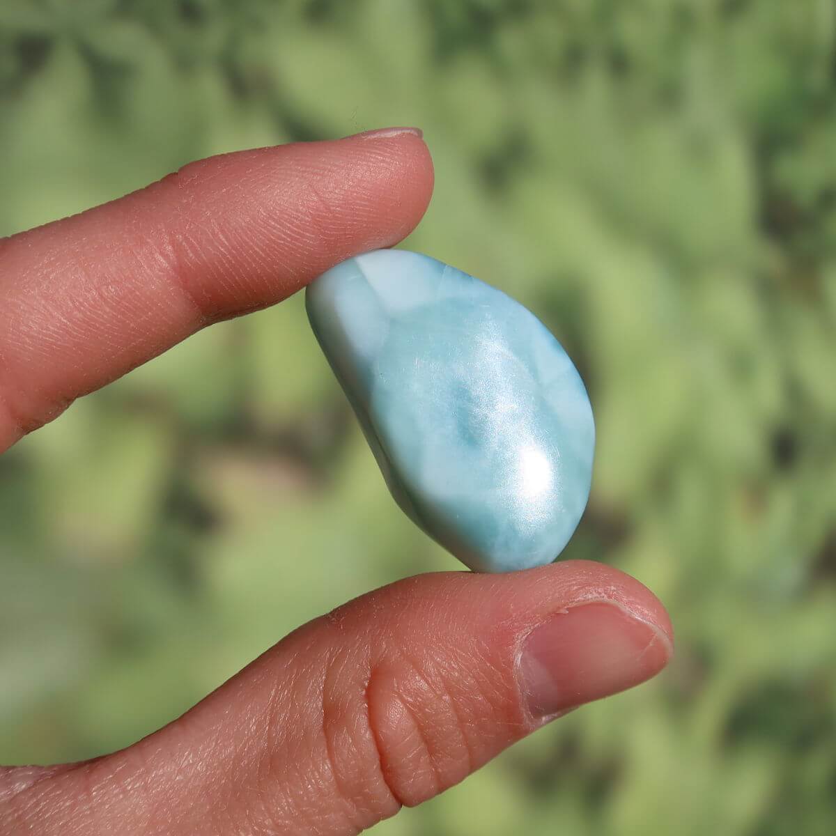 Person holding a polished Larimar stone against a blurred green background, showcasing its natural blue hue and smooth surface.