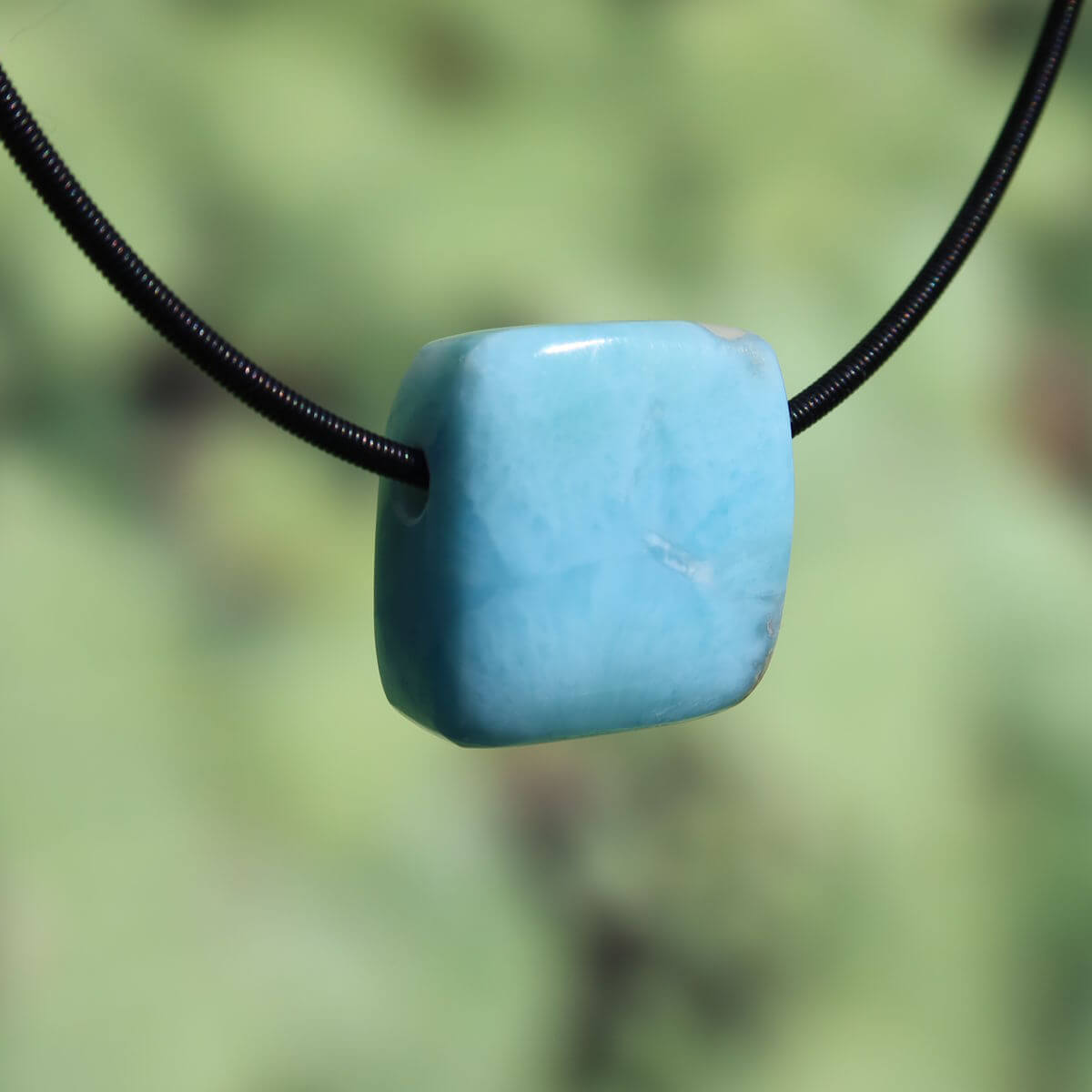 Square-shaped Larimar pendant on a black cord, showcasing a light blue stone with natural patterns, emphasizing rarity and craftsmanship.