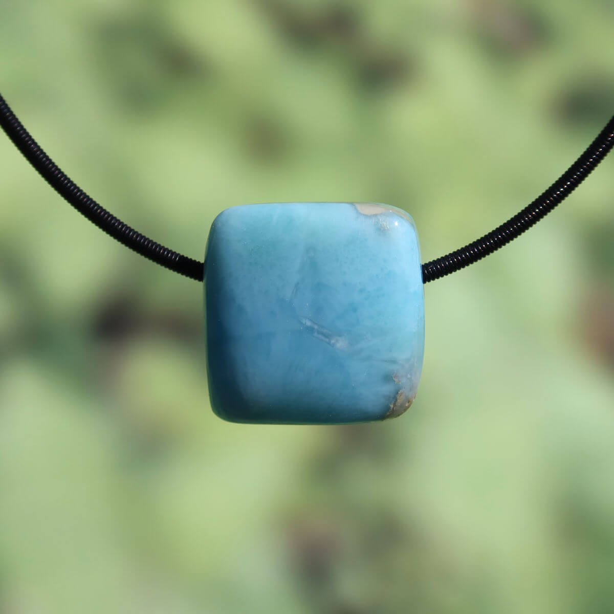 Square-shaped Larimar pendant on a black cord, showcasing a light blue stone with natural patterns, emphasizing rarity and craftsmanship.