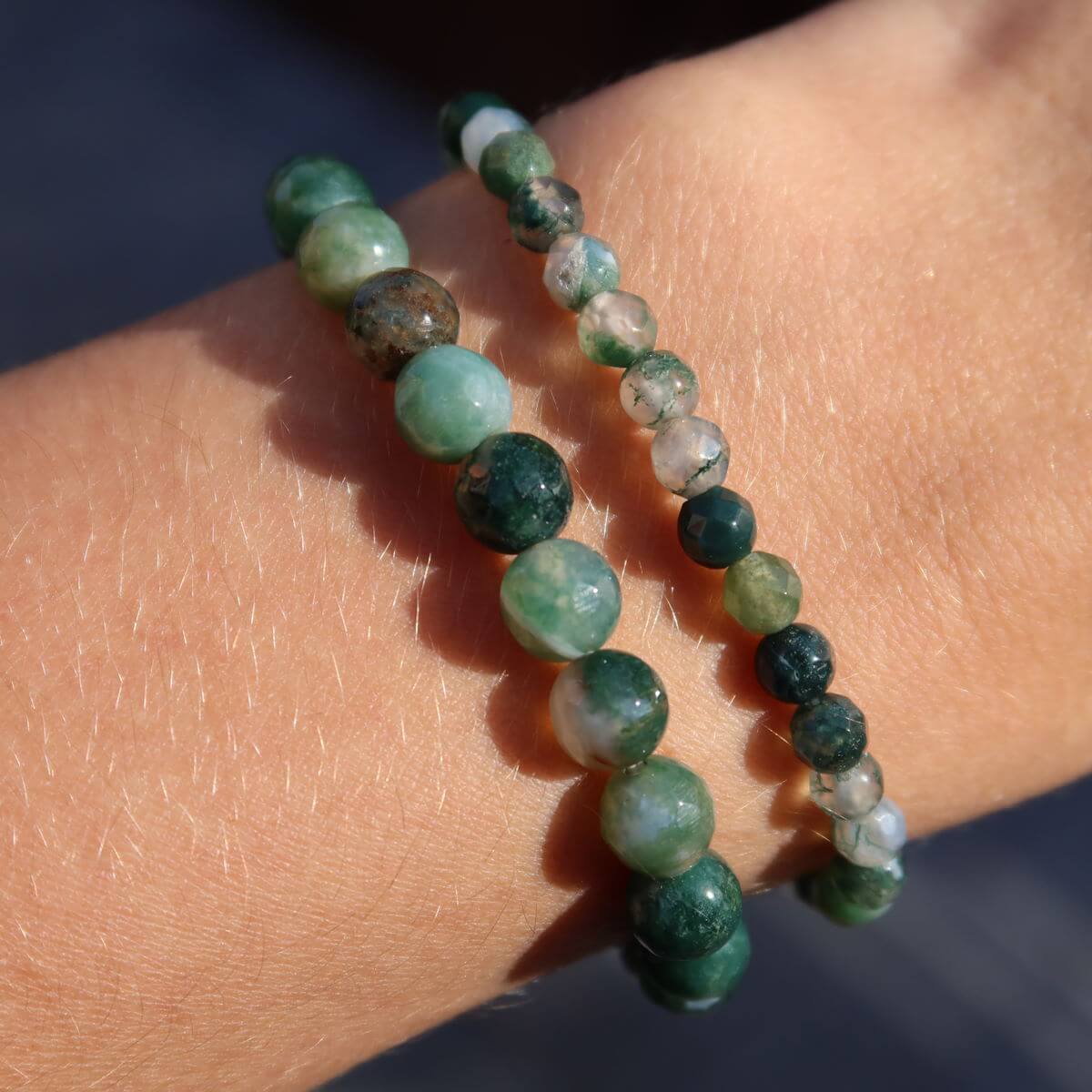 Close-up of faceted moss agate gemstone bracelet in various shades of green, worn on wrist, emphasizing its unique patterns.