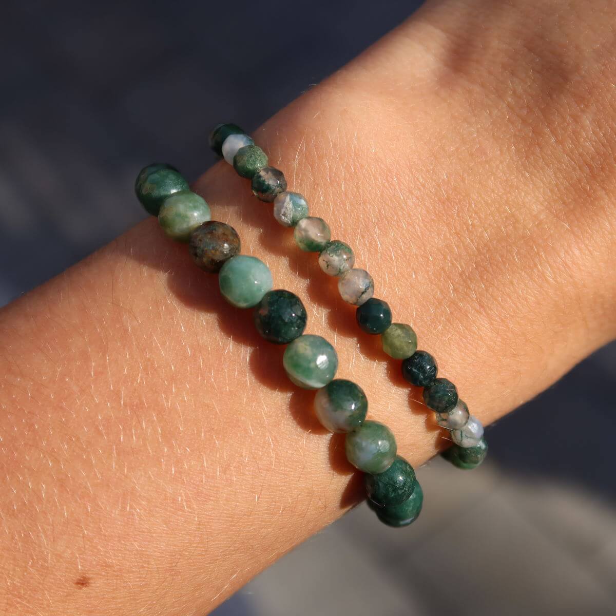 Close-up of faceted moss agate gemstone bracelet in various shades of green, worn on wrist, emphasizing its unique patterns.