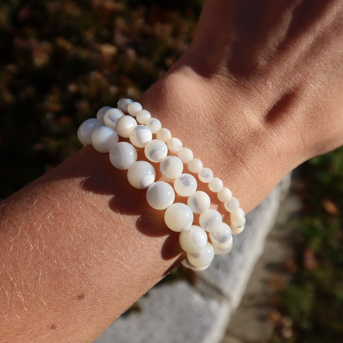 Person trägt Perlmutt Edelstein Armband - 1 Stück - in Varianten 4-6-8 oder 10mm mit sanftem Schillern auf ihrem Handgelenk.
