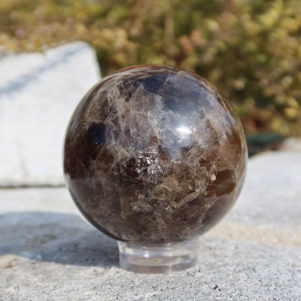 Rauchquarz Kugel geschliffen auf Steinwand vor Naturkulisse, erhältlich bei Steinwelten Graz und Wiener Neustadt.