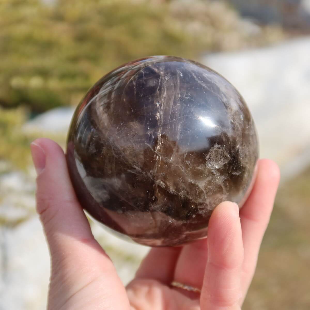 Rauchquarz Kugel geschliffen auf Steinwand vor Naturkulisse, erhältlich bei Steinwelten Graz und Wiener Neustadt.