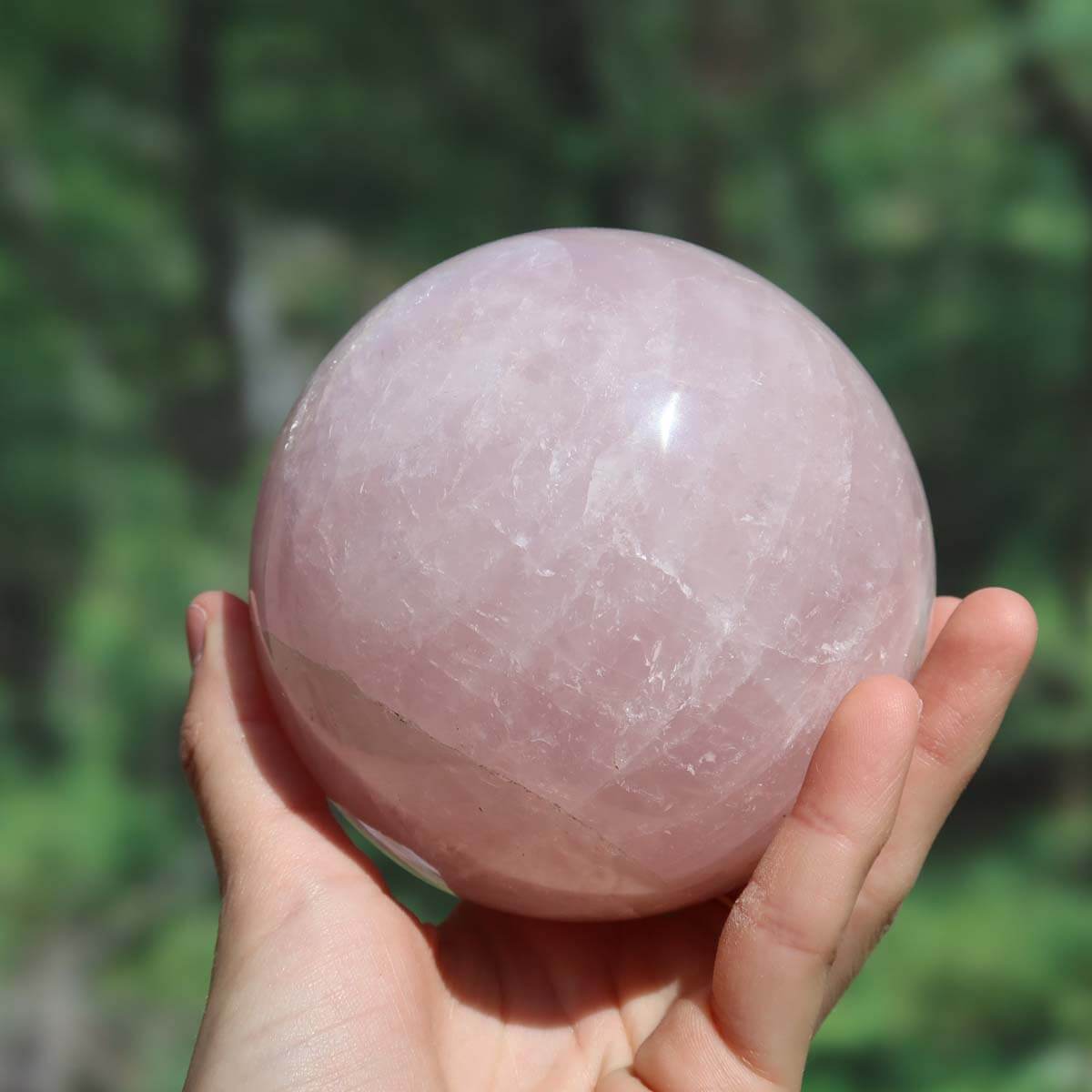 Hand holding 95mm polished rose quartz sphere, known as the Stone of Love, ideal for creating a harmonious atmosphere in any room.