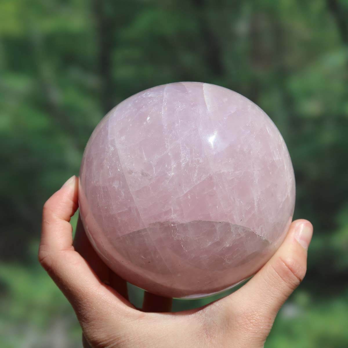 Hand holding 95mm polished rose quartz sphere, known as the Stone of Love, ideal for creating a harmonious atmosphere in any room.