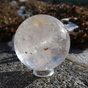 Rutilquarz Kugel – Natürliche Kristallkugel - 80mm Durchmesser Nr. 26 mit goldenen Rutilnadeln auf steinigem Hintergrund