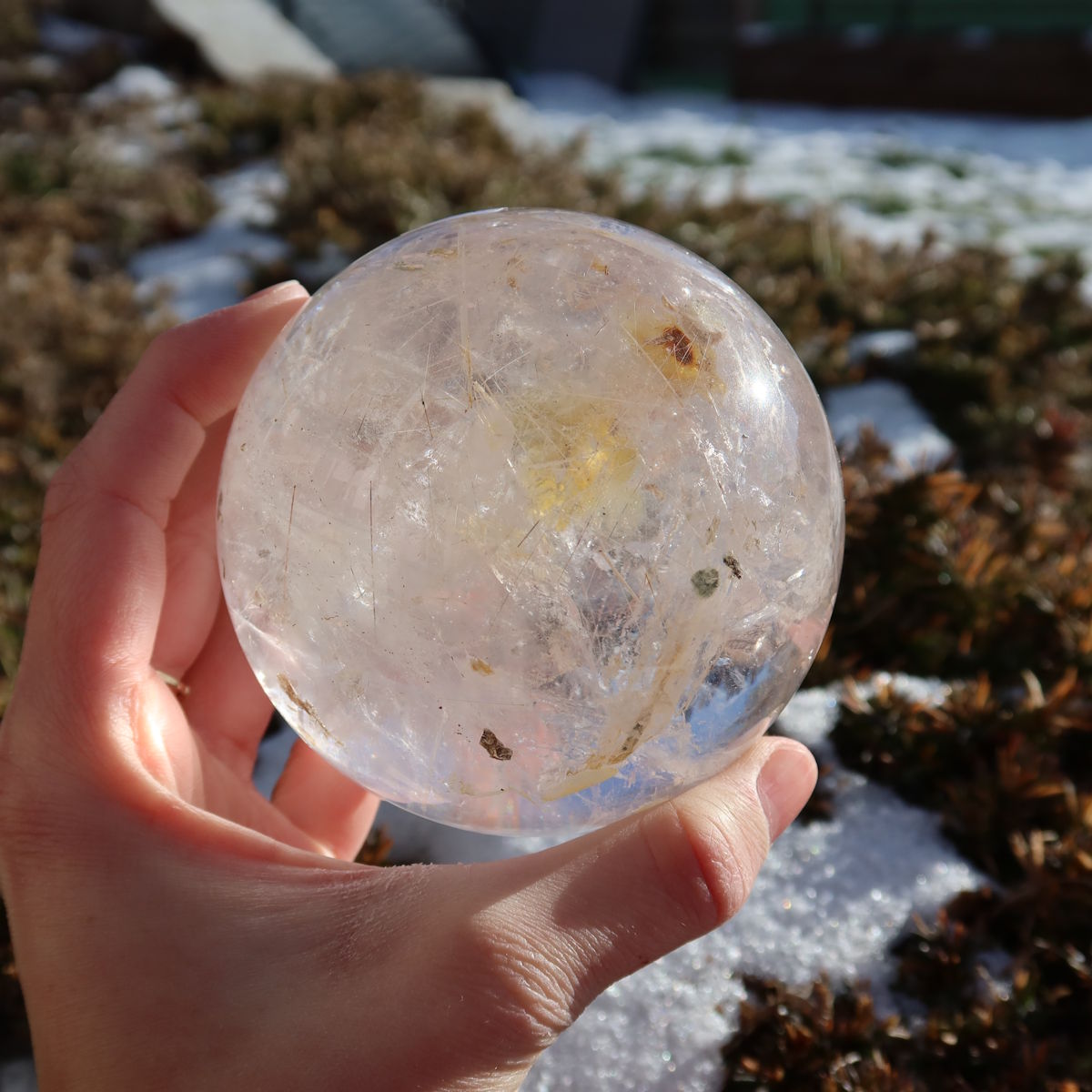 Rutilquarz Kugel – Natürliche Kristallkugel - 80mm Durchmesser Nr. 26 mit goldenen Rutilnadeln in einer Hand im Freien gehalten