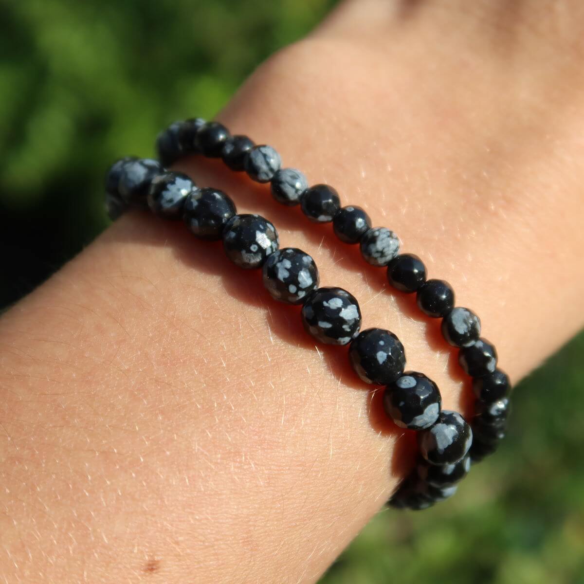 Faceted snowflake obsidian gemstone bracelet with black and white patterns displayed on a wrist.