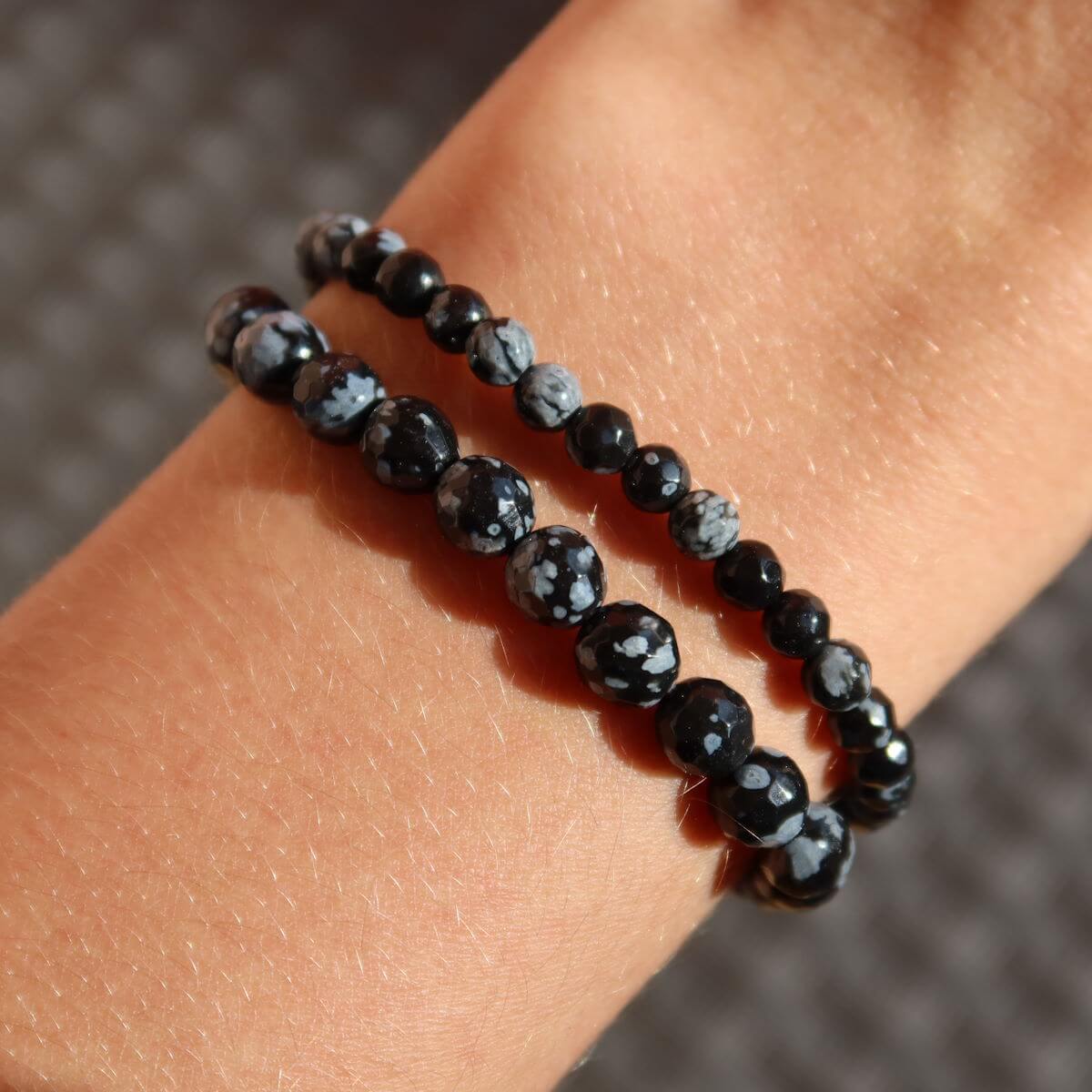 Faceted snowflake obsidian gemstone bracelet with black and white patterns displayed on a wrist.