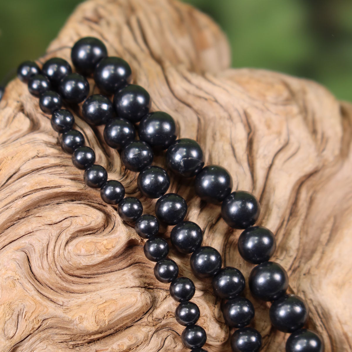 Schungit-Edelsteinstrang zur Schmuckherstellung auf Holz dargestellt, bereit für Ketten oder Armbänder.