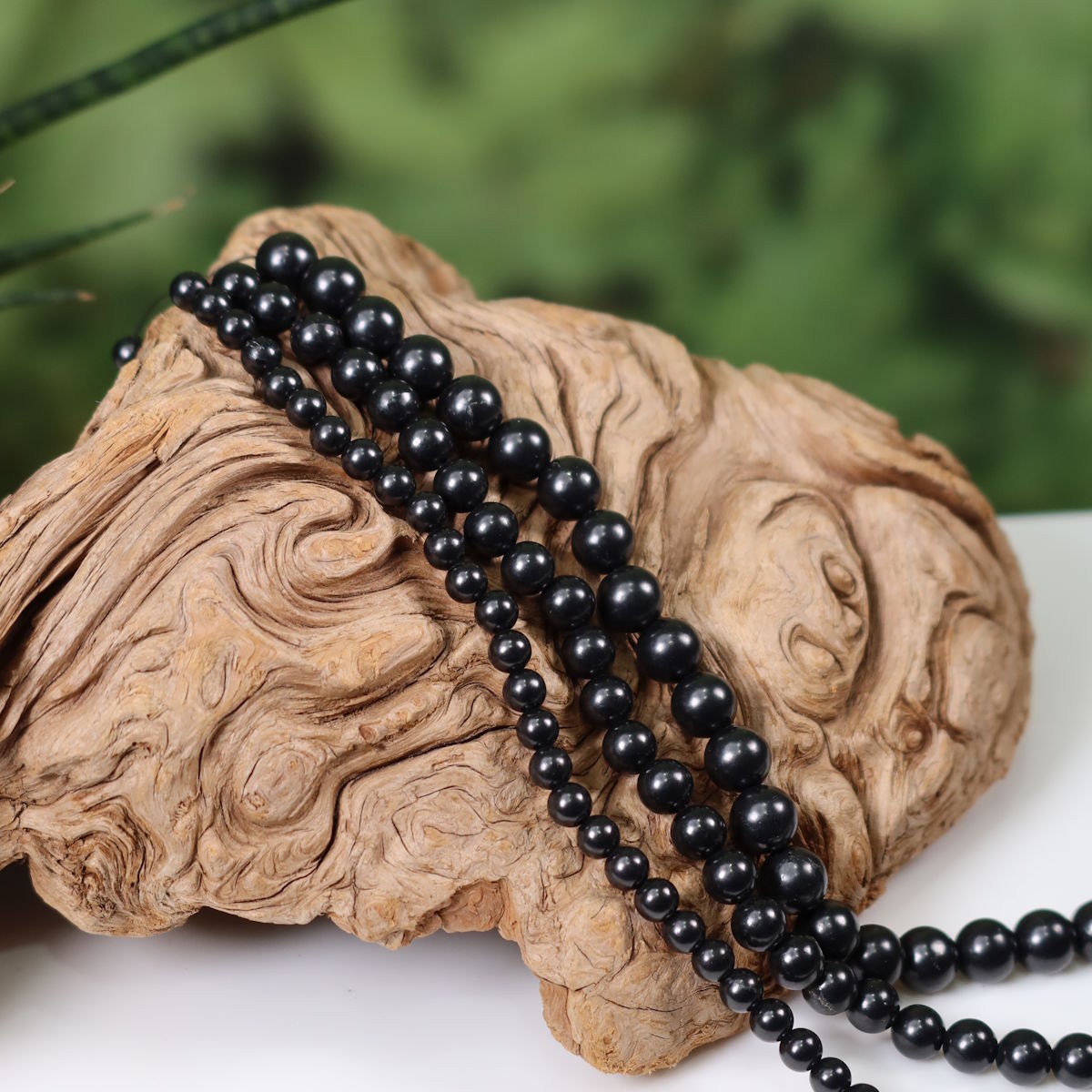 Schungit-Edelsteinstrang zur Schmuckherstellung auf Holz dargestellt, bereit für Ketten oder Armbänder.