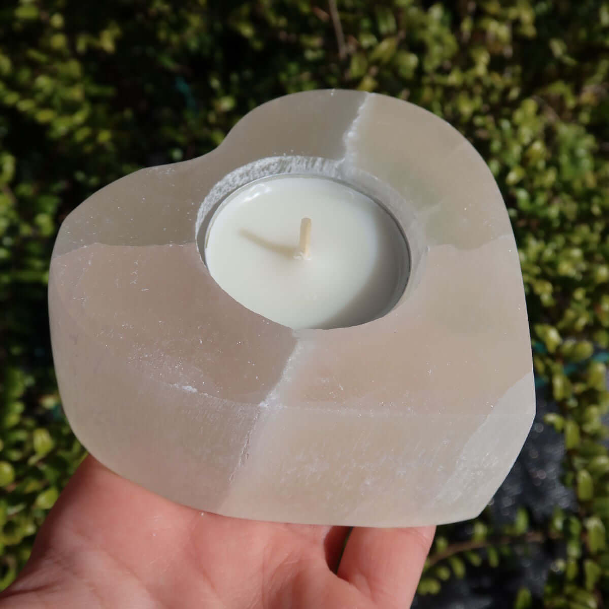 Heart-shaped selenite tealight holder, 9cm, natural mineral from Morocco, polished finish, hand-holding, outdoor setting.