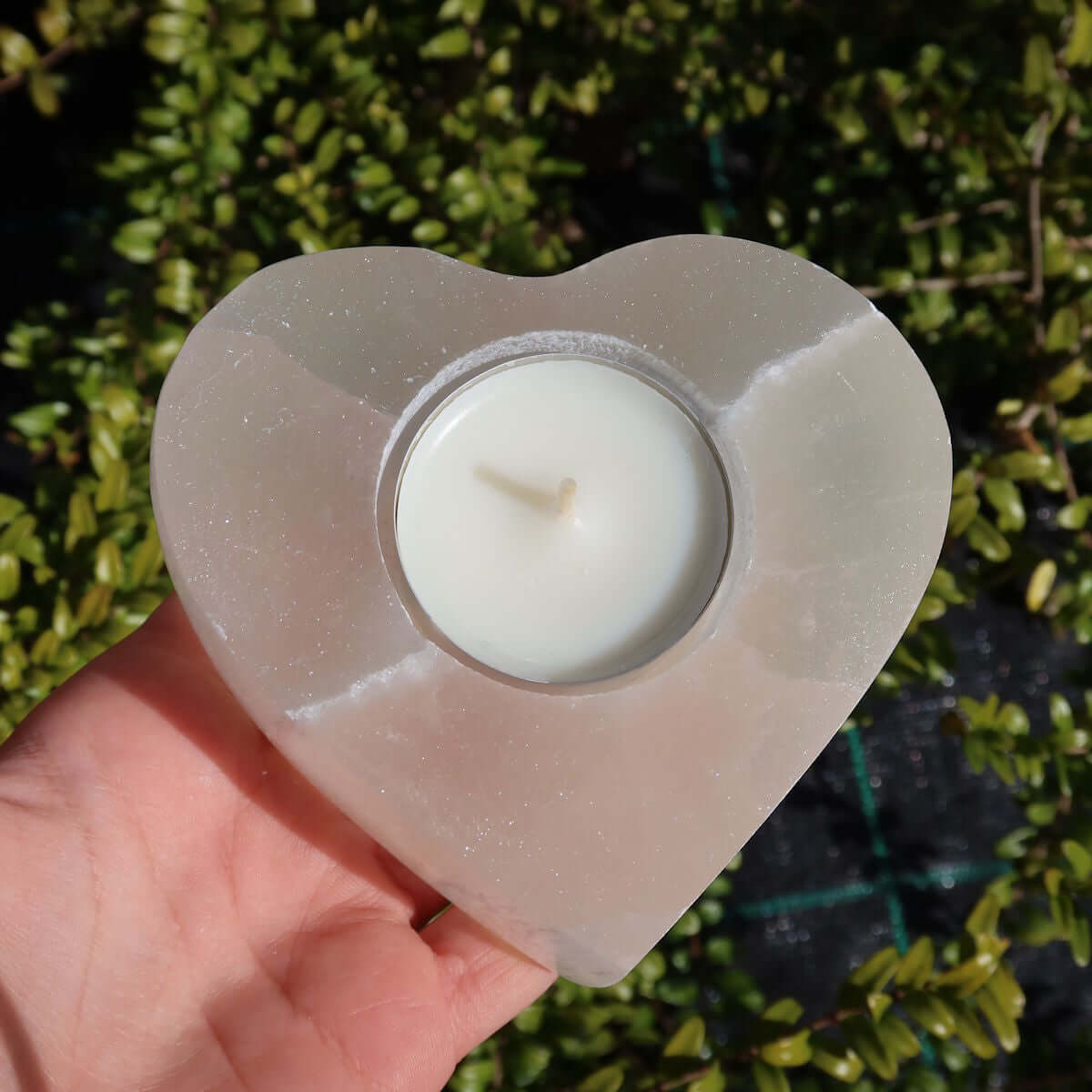 Heart-shaped selenite tealight holder, 9cm, natural mineral from Morocco, polished finish, hand-holding, outdoor setting.