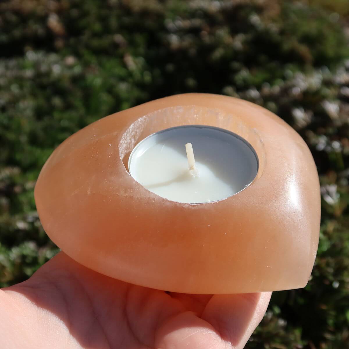 Selenit Teelichthalter in Herzform orange, 9cm, Lichtbringer und Schutzstein, auf Hand im Freien präsentiert.