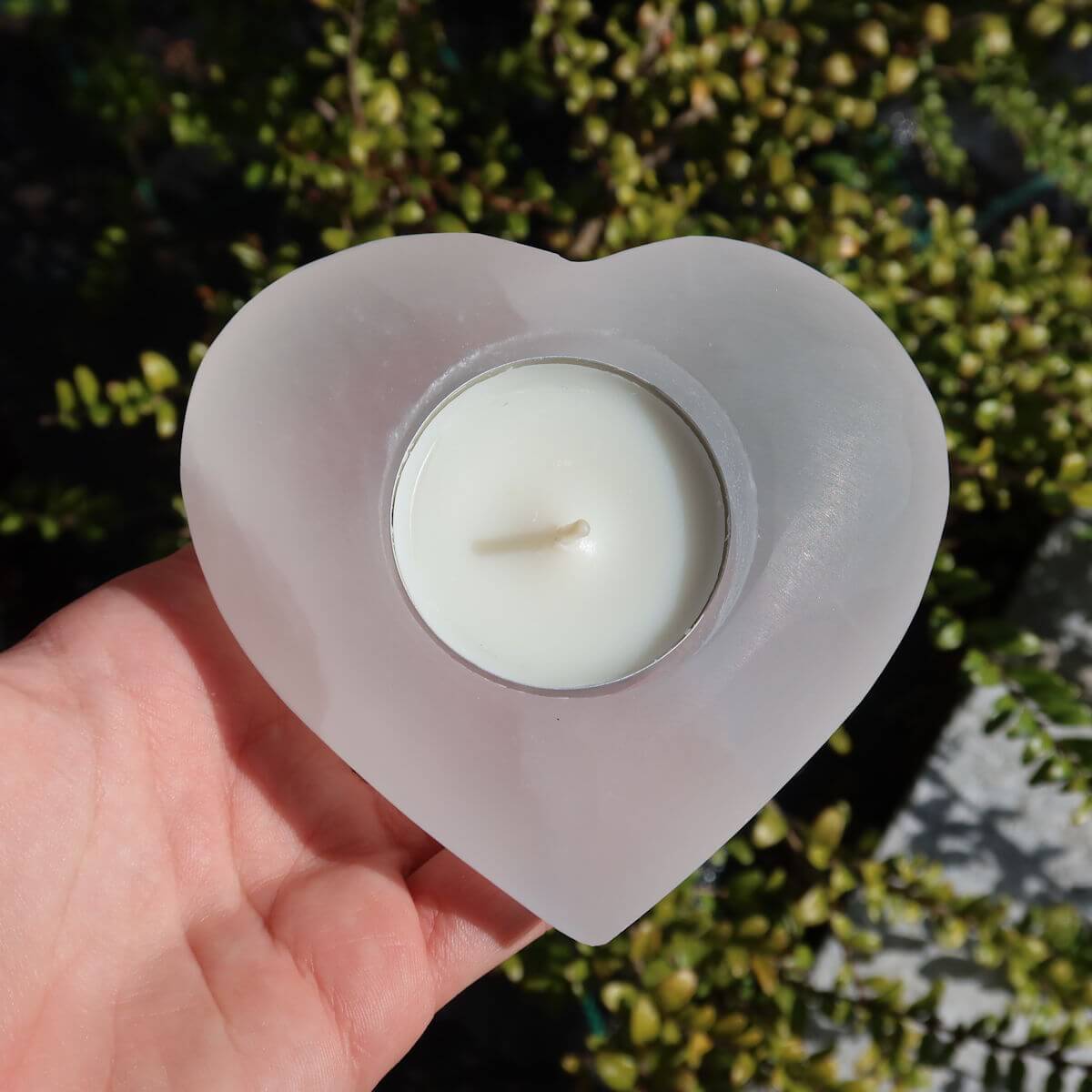 Heart-shaped white selenite tealight holder held in hand, used for stress relief and protection.