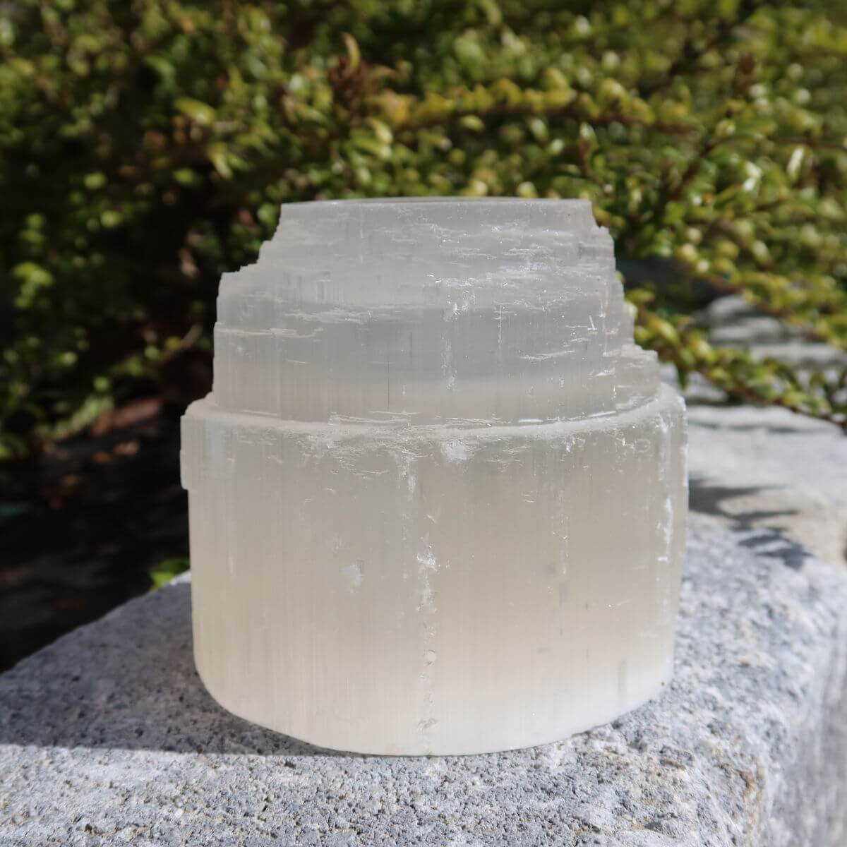 Natürlicher Selenit Kristall Teelicht 8cm auf Stein im Freien, bekannter Lichtbringer und Schutzstein für Stabilität und Stressabbau.