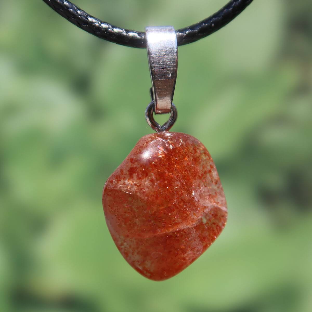 Natürlicher Sonnenstein Anhänger mit Silberschlaufe, 20mm, in warmen Gold-Orange Tönen, Unikat Nr. 2, auf grünem Hintergrund.