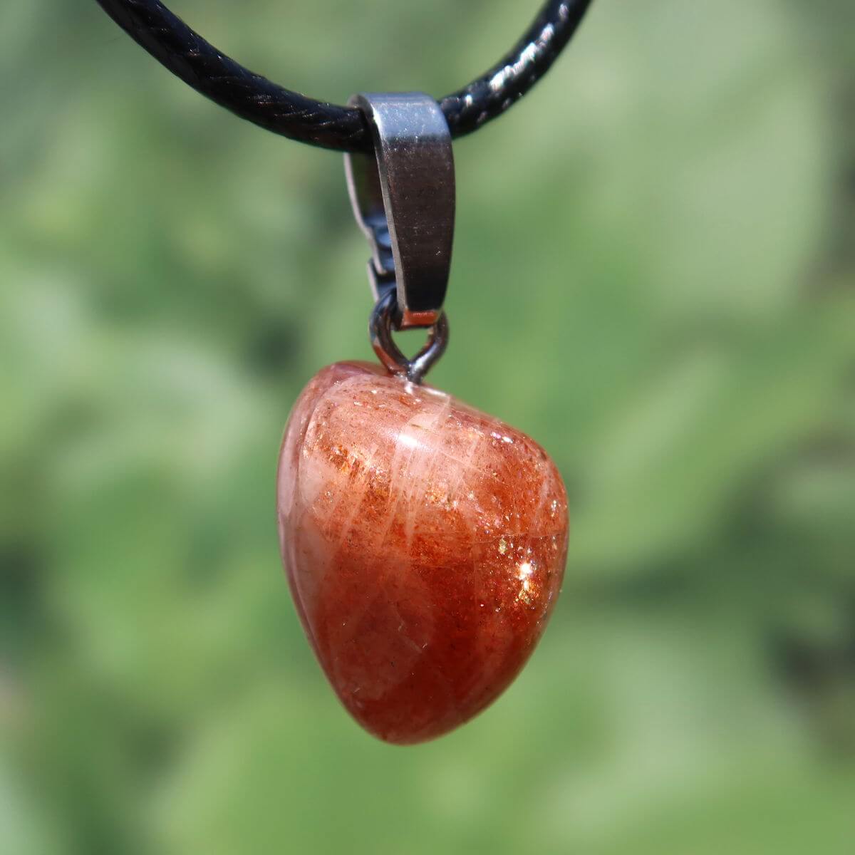 Polished natural sunstone pendant with silver loop against green background, promoting positivity and reducing anxiety.