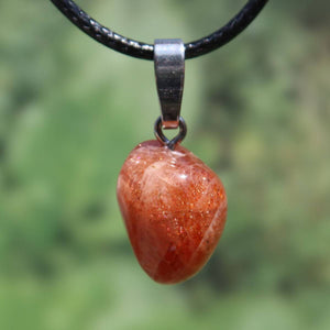 Polished natural sunstone pendant with silver loop against green background, promoting positivity and reducing anxiety.
