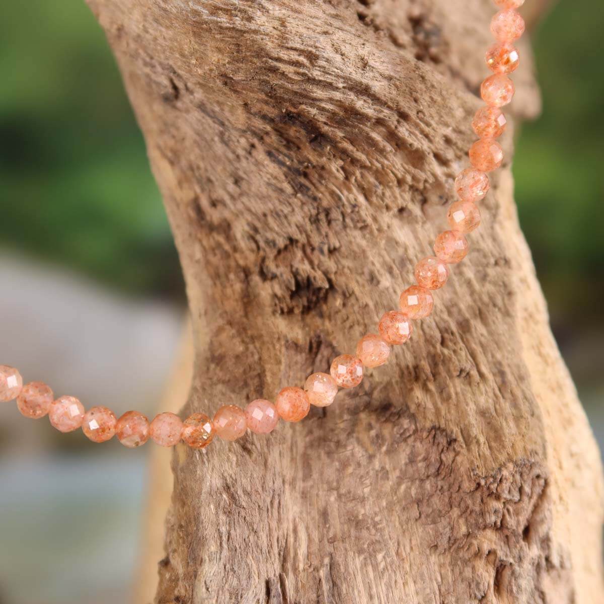 Sonnenstein facettierte Edelsteinkette 42cm mit Pfirsich-Schimmer auf Holz ausgestellt - Steinwelten kaufen online.