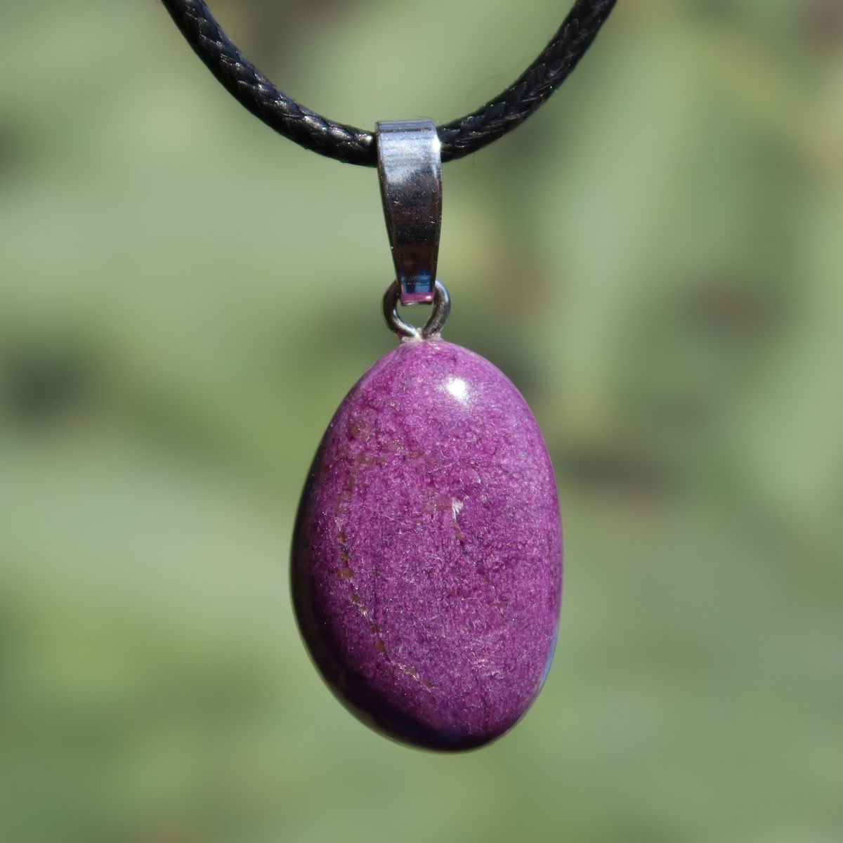 Natürlicher Stichtit Anhänger 25mm - innere Ruhe und Gelassenheit - UNIKAT Nr. 5, lila Stein an schwarzer Kette vor grünem Hintergrund