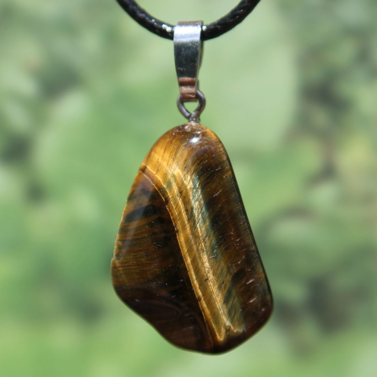 Tigerauge Anhänger 30mm - Selbstbewusstsein und Konzentration - UNIKAT Nr. 12, glänzender Edelstein mit Silberöse vor grünem Hintergrund