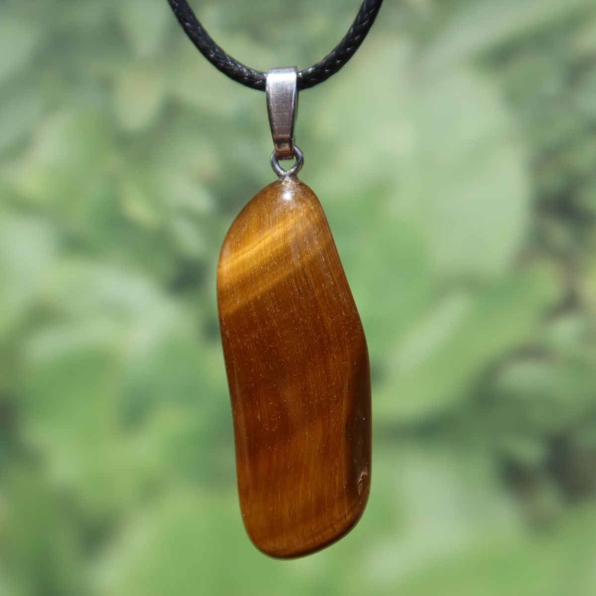 Tigerauge Anhänger 45mm - Selbstbewusstsein und Konzentration - UNIKAT Nr. 13, braunes Edelstein-Schmuckstück mit Silberöse auf grünem Hintergrund