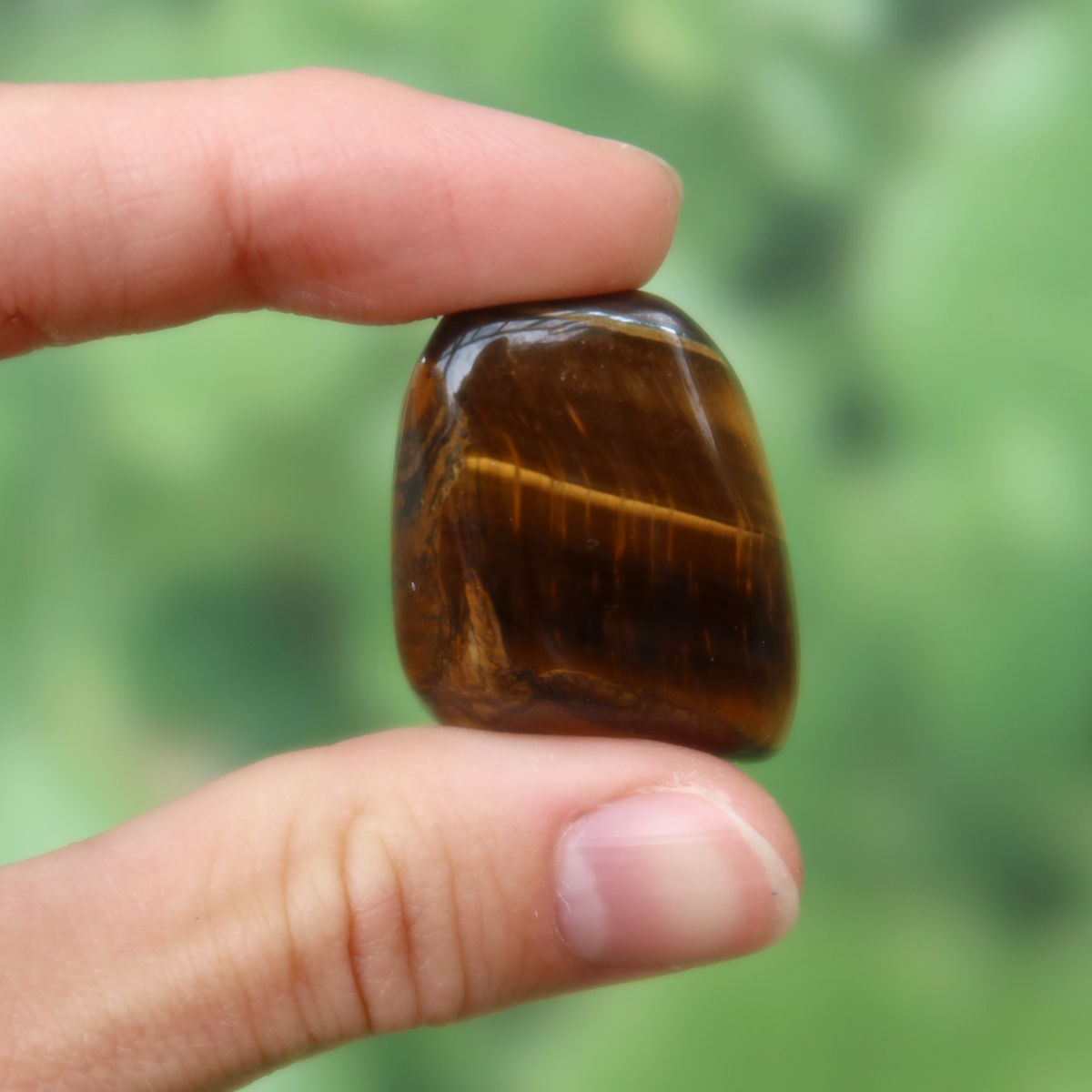 Tigerauge Handschmeichler 30mm - Selbstbewusstsein und Konzentration - Unikat Nr. 22 in einer Hand gehalten, zeigt glänzende Streifen.