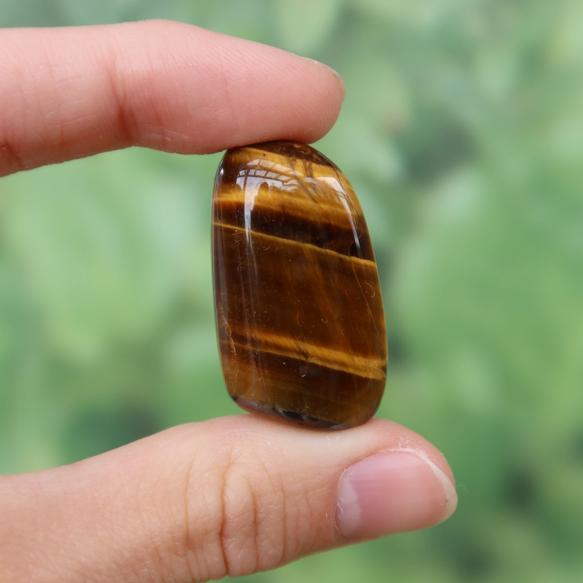 Tigerauge Handschmeichler 34mm - Selbstbewusstsein und Konzentration - Unikat Nr. 27, glänzender brauner Stein mit Streifen gehalten in der Hand