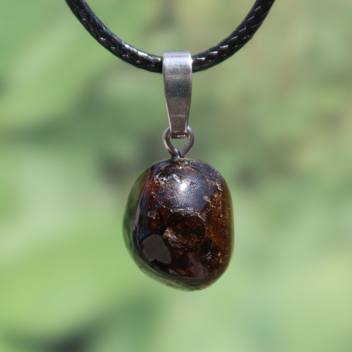 Turmalin Dravit Anhänger mit Silberschlaufe, tiefbrauner Edelstein, Schmuckstück auf grünem Hintergrund, strahlt Kraft und Ruhe aus.