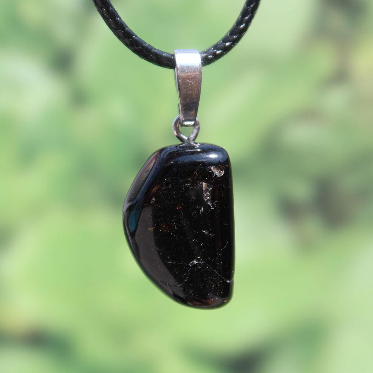 Turmalin Dravit Anhänger mit Silberschlaufe, brauner Edelstein Schmuck für Selbstsicherheit und Entspannung vor grünem Hintergrund