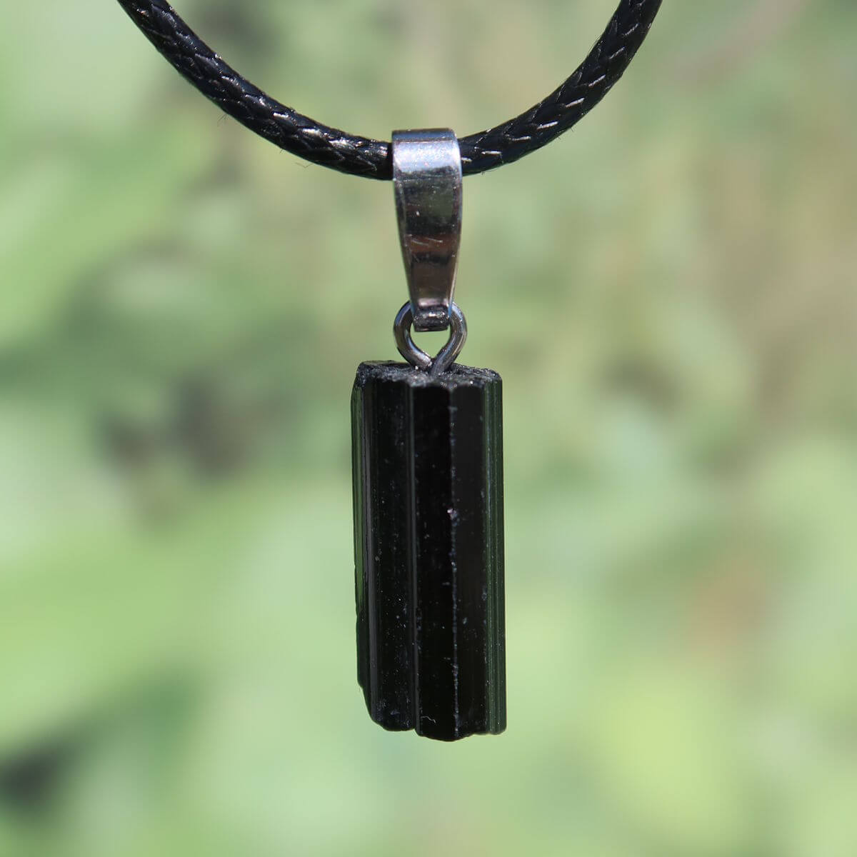 Black tourmaline schörl pendant with silver loop, unique design, 21mm, symbol of protection and clarity against green blurred background.