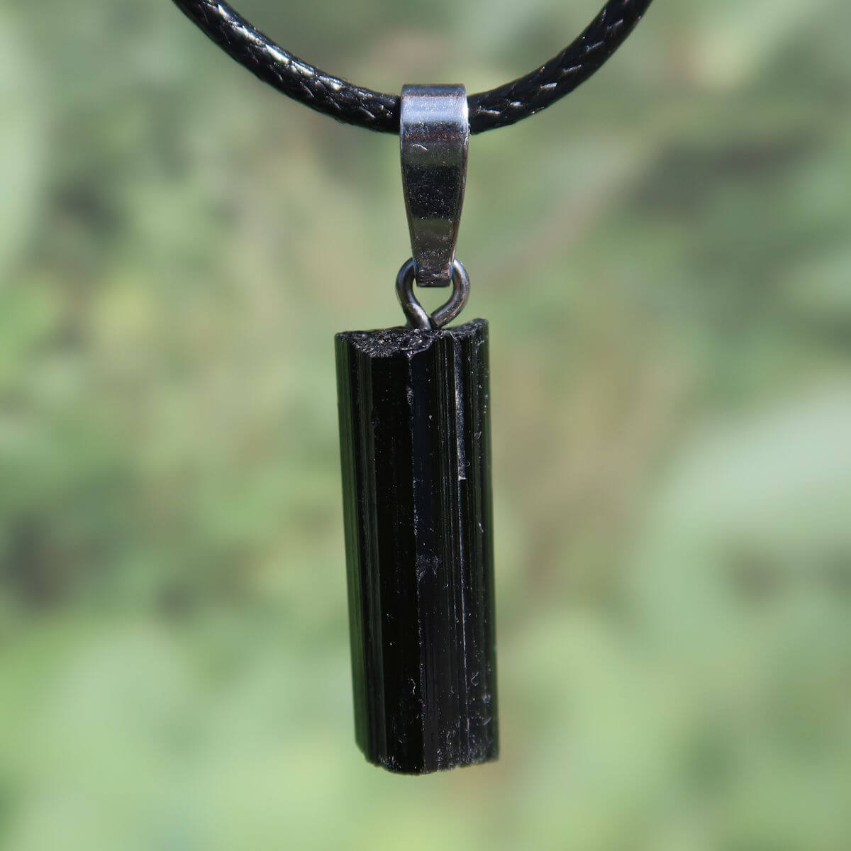 Black tourmaline pendant with silver loop for protection and uniqueness, 24mm, on a black cord, close-up view.
