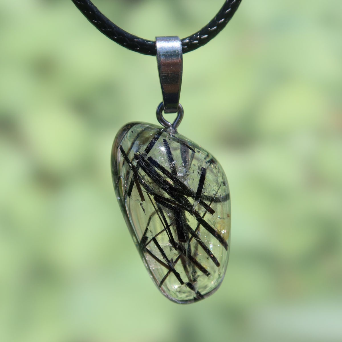 Turmalinquarz pendant with black tourmaline inclusions on a leather cord, unique gemstone for protection and tranquility, against green background