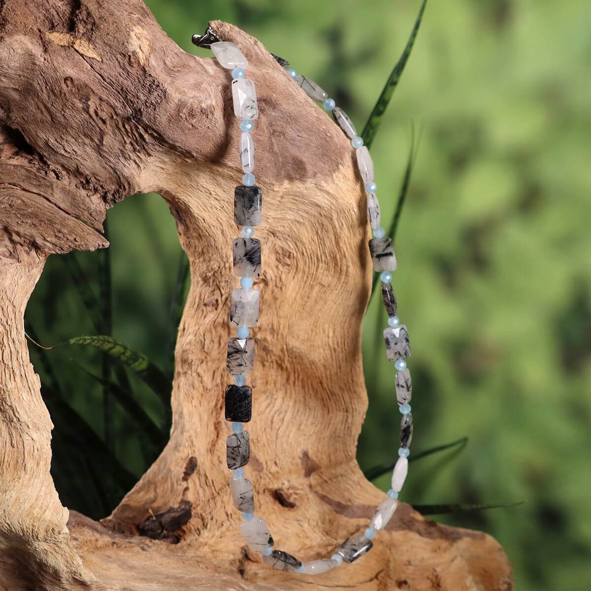 Handcrafted necklace with tourmaline quartz and aquamarine on a wooden display, offering a modern and natural look.