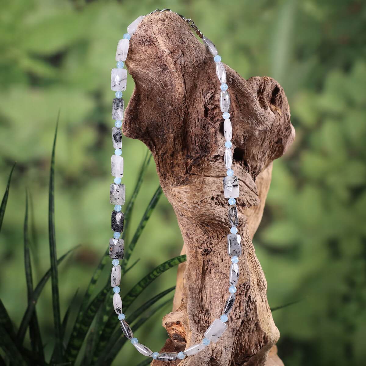 Handcrafted necklace with tourmaline quartz and aquamarine on a wooden display, offering a modern and natural look.