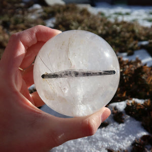 Hand hält Turmalinquarz Kugel – natürliche Kristallkugel Nr. 25 mit schwarzen Turmalin Einschlüssen in natürlichem Licht.