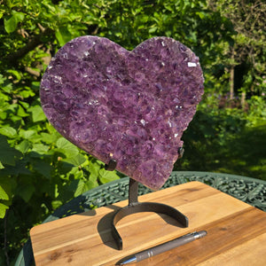 Amethyst Druse Amethyst Geode in Herzform mit Metallsockel 31x28x12cm - NR-24 auf einem Holztisch mit Stift
