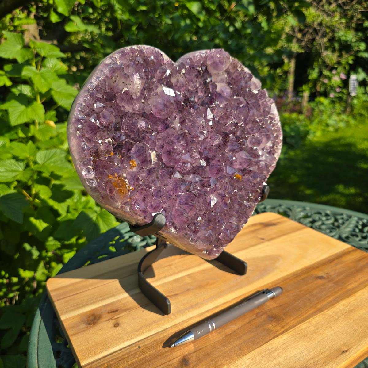 Amethyst Druse Amethyst Geode in Herzform mit Metallsockel 26x24x14cm - NR-21 auf einem Tisch im Freien.