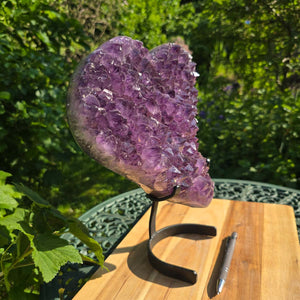 Amethyst Druse Amethyst Geode in Herzform mit Metallsockel 31x28x12cm - NR-24 auf einem Stand in der Natur.