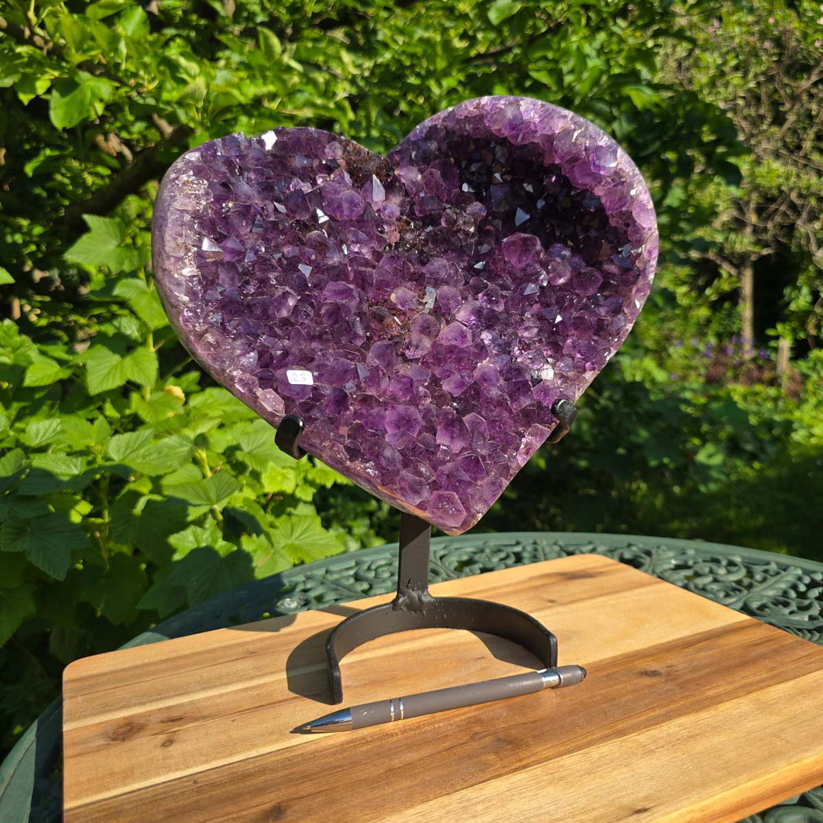Amethyst Druse Amethyst Geode in Herzform mit Metallsockel 32x28x14cm - NR-23 auf einem stabilen Halter im Freien.