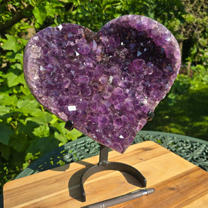 Amethyst Druse Amethyst Geode in Herzform mit Metallsockel 32x28x14cm - NR-23 auf einem stabilen Halter im Freien.