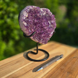 Amethyst Druse Amethyst Geode in Herzform mit Metallsockel 19x16x10cm - NR-63 auf einem Holztisch mit Stift